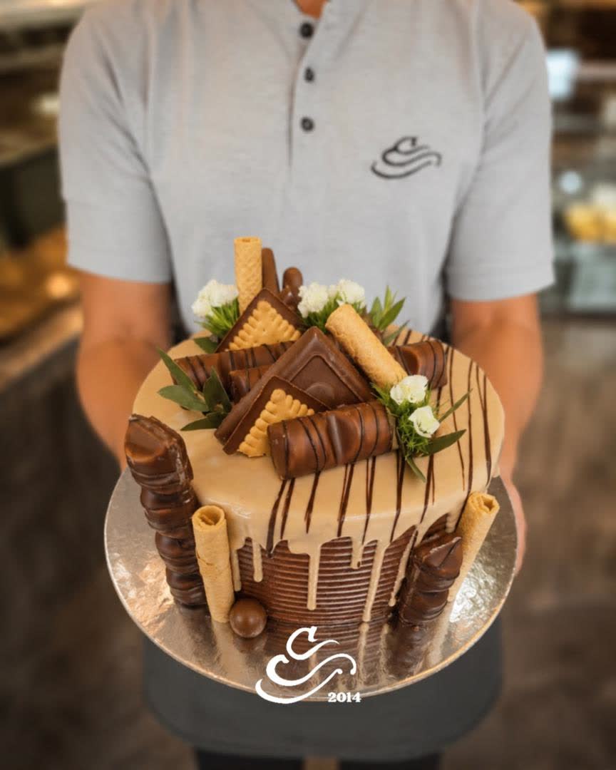 Bolo alto decorado com chocolate, segurado por um pasteleiro da casa